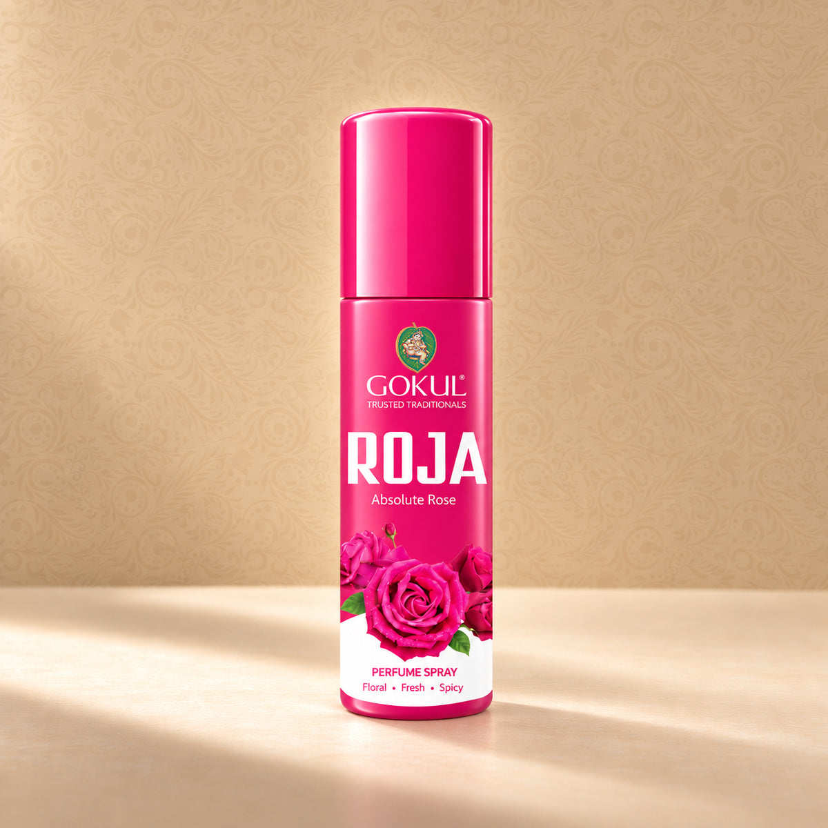 A bottle of Gokul Perfumes ROJA Absolute Rose perfume spray, featuring a vibrant pink cap and label with rose graphics, set against a warm beige patterned background.